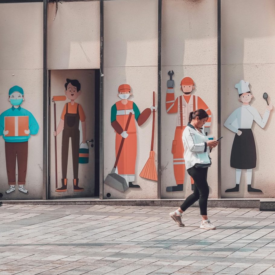 Junge Frau geht an einer Wand mit Illustrationen von verschiedenen Handwerkern vorbei. BU - Berufsstatus & Berufsgruppen