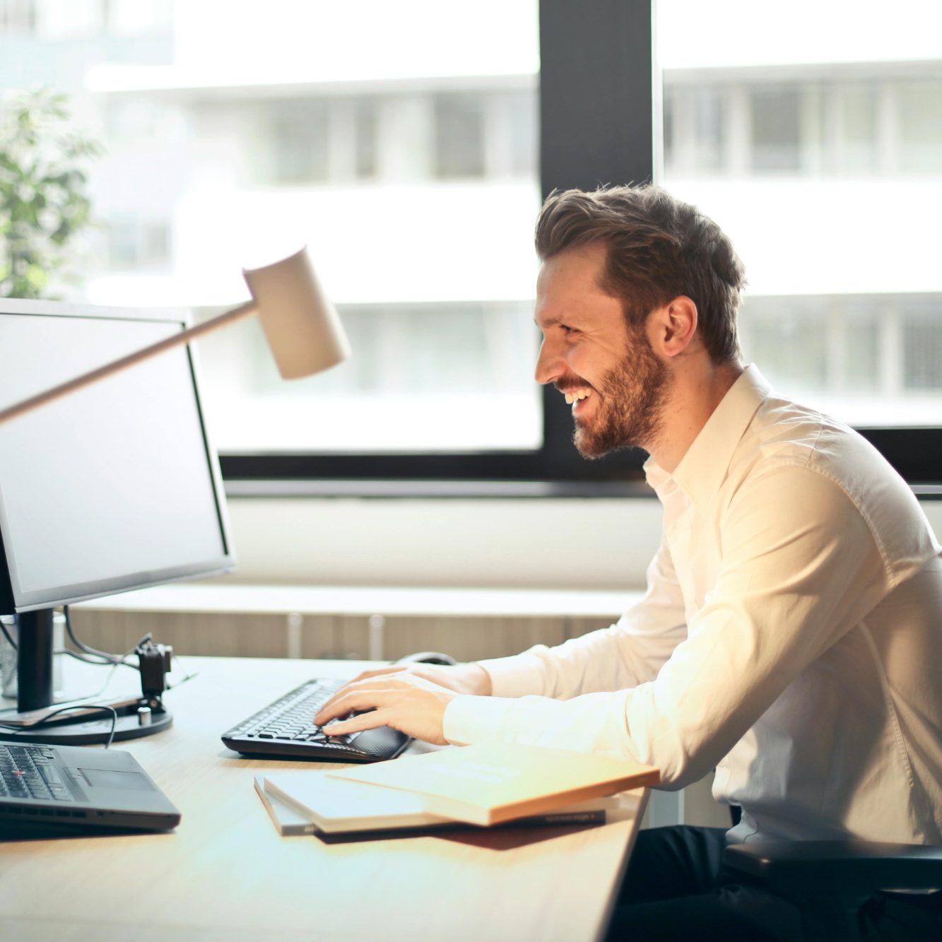 Mann sitzt am Schreibtisch, lächelt und arbeitet an zwei Monitoren.