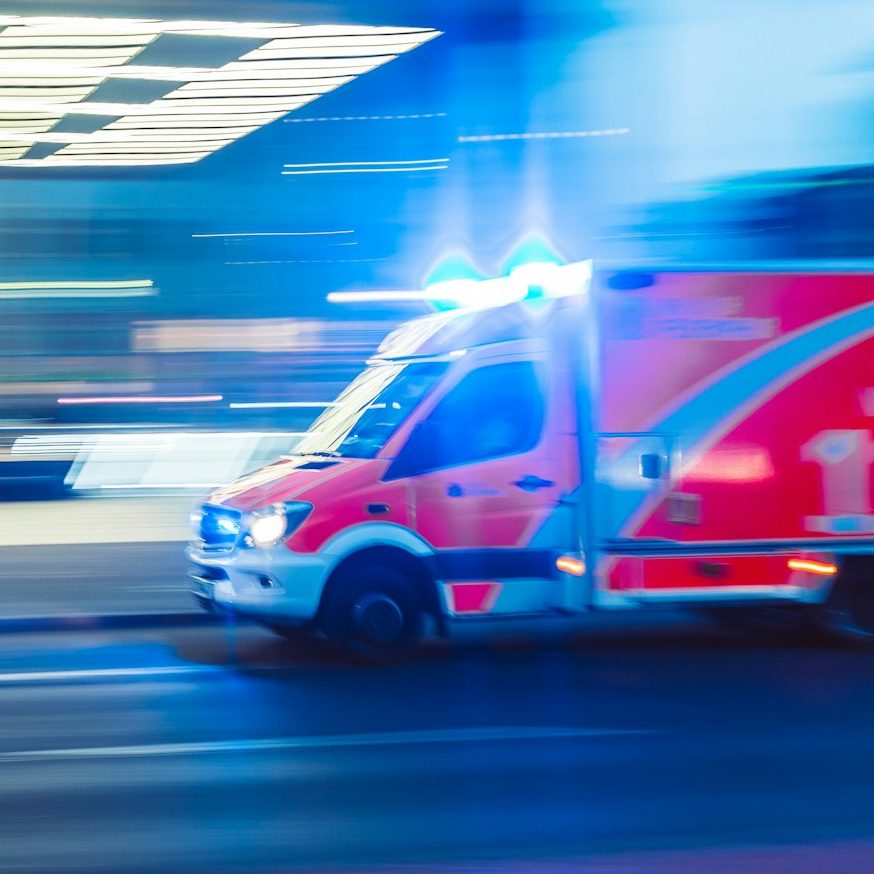 BU für den öffentlichen Dienst Ein Rettungswagen mit blinkenden Lichtern fährt schnell durch die Stadt zur Berufsunfähigkeitsversicherung