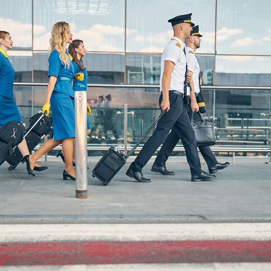 BU für Piloten und Flugbegleiter Gruppe von Flugbegleitern und Piloten, die mit Gepäck zum Terminal gehen zur Berufsunfähigkeitsversicherung