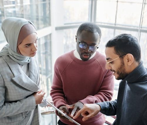 Drei Personen diskutieren in einem modernen Büro über ein digitales Gerät. Ratgeber für Berufsunfähigkeitsversicherung (BU)