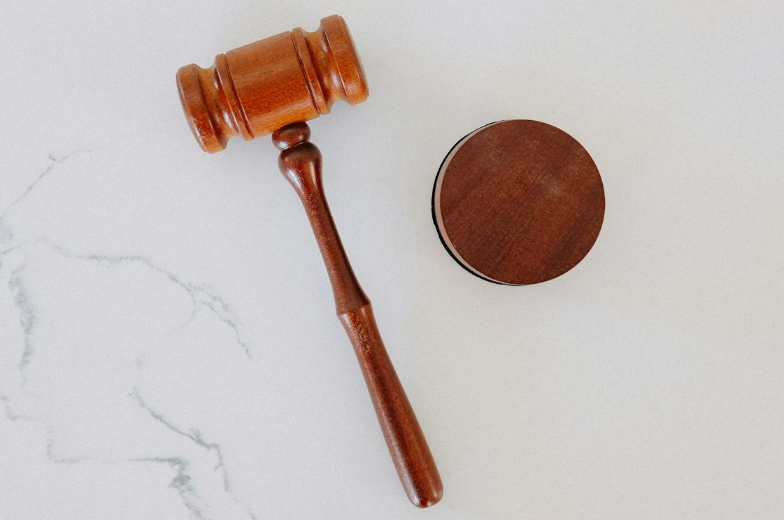 Prozessquote in der Berufsunfähigkeitsversicherung Ein Holzhammer und ein runder, brauner Stempel auf einem weißen Untergrund für die Prozessquote in der Berufsunfähigkeitsversicherung