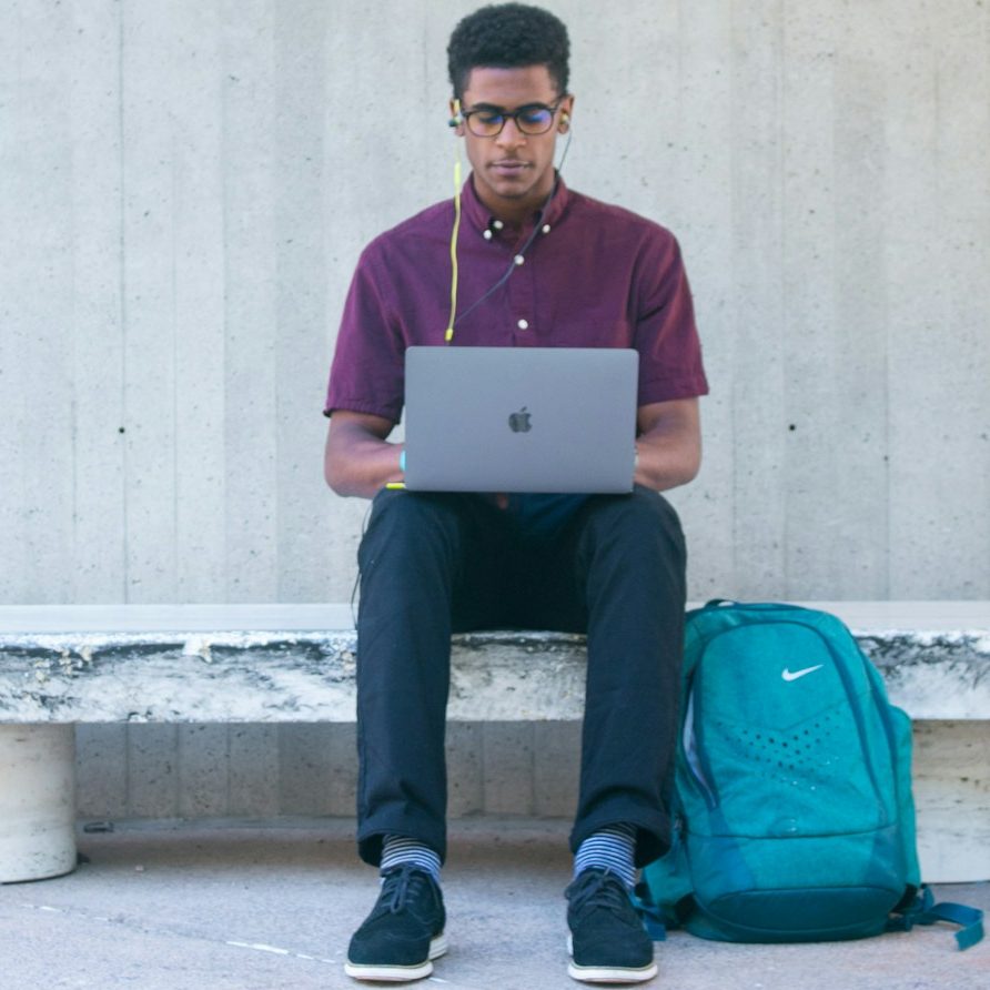 BU für Auszubildende Junger Mann mit Brille arbeitet am Laptop, Rucksack neben ihm auf einer Bank zur Berufsunfähigkeitsversicherung