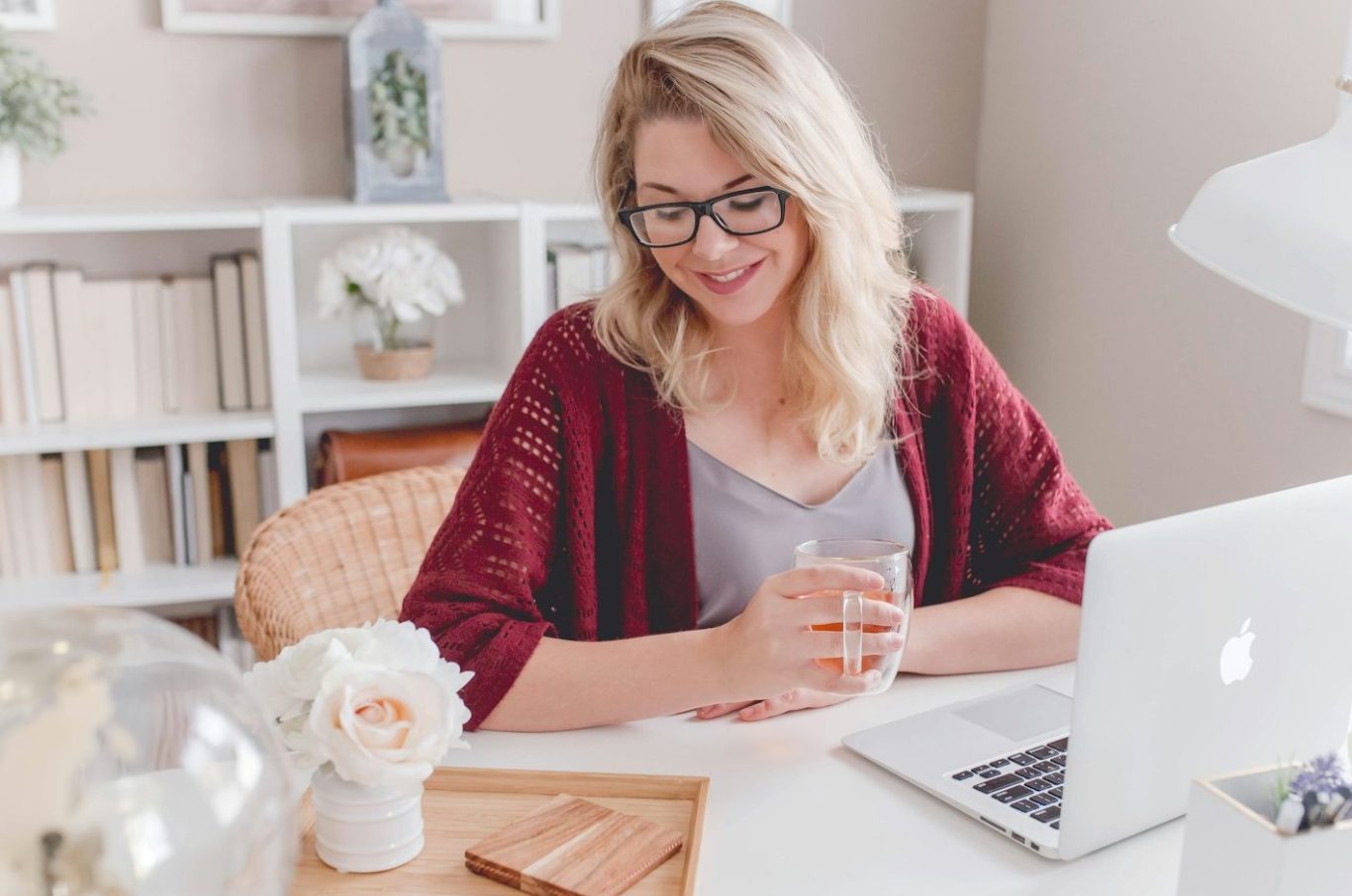 Lächelnde Frau mit Brille, sitzend am Schreibtisch mit Tasse in der Hand und schaut sich am Laptop die Leistungsquoten von BU-Versicherer an