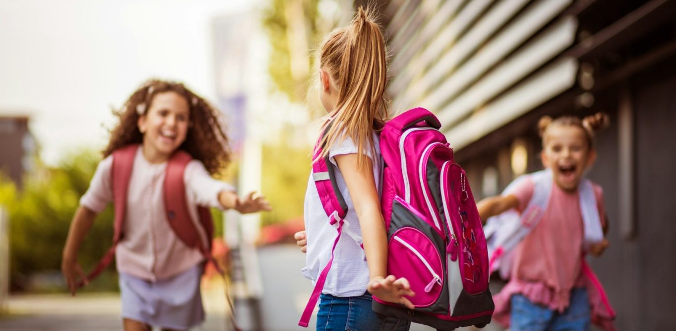 BU für Schüler und Kinder Drei Mädchen mit Rucksäcken rennen fröhlich auf einen Weg zu. BU für Schüler und Kinder
