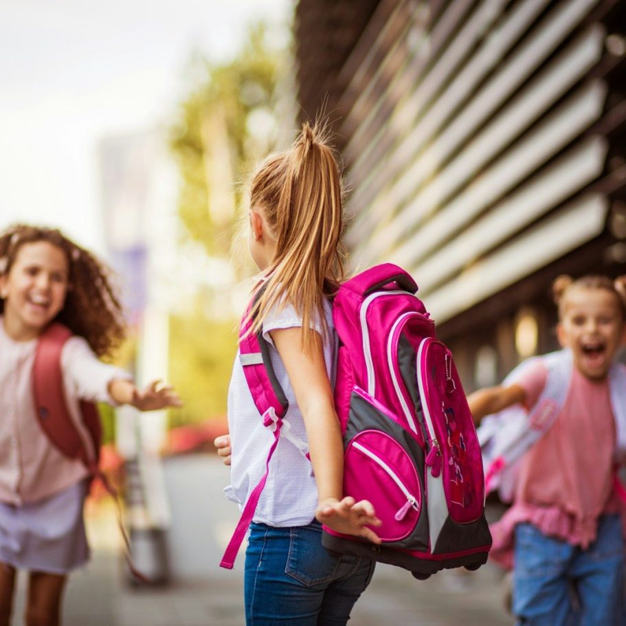 BU für Kinder und Schüler Drei Kinder mit Rucksäcken spielen fröhlich im Freien.