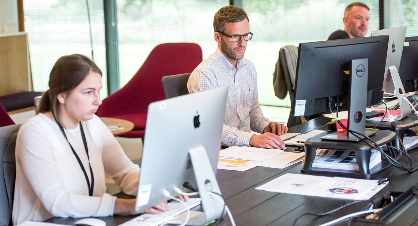 BU für Kaufleute und Büroberufe Drei Personen arbeiten an Computern in einem modernen Büro mit großen Fenstern. BU für Kaufleute und Büroberufe