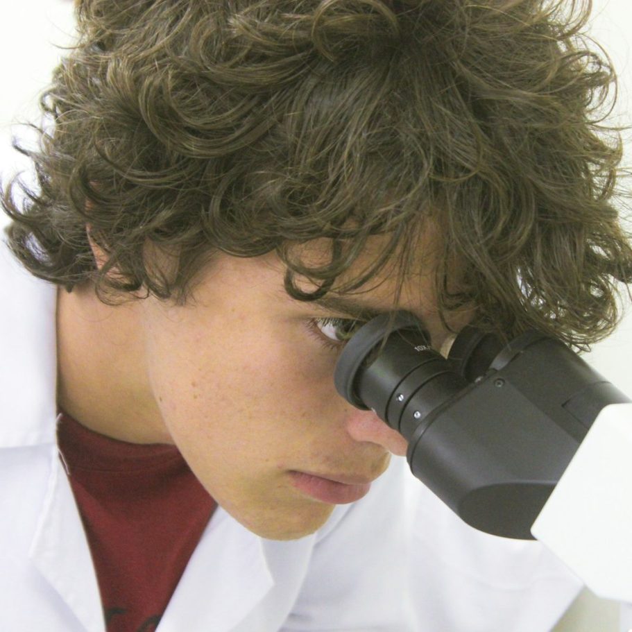 BU für MINT-Berufe Junger Mensch mit lockigem Haar schaut durch ein Mikroskop zur Berufsunfähigkeitsversicherung