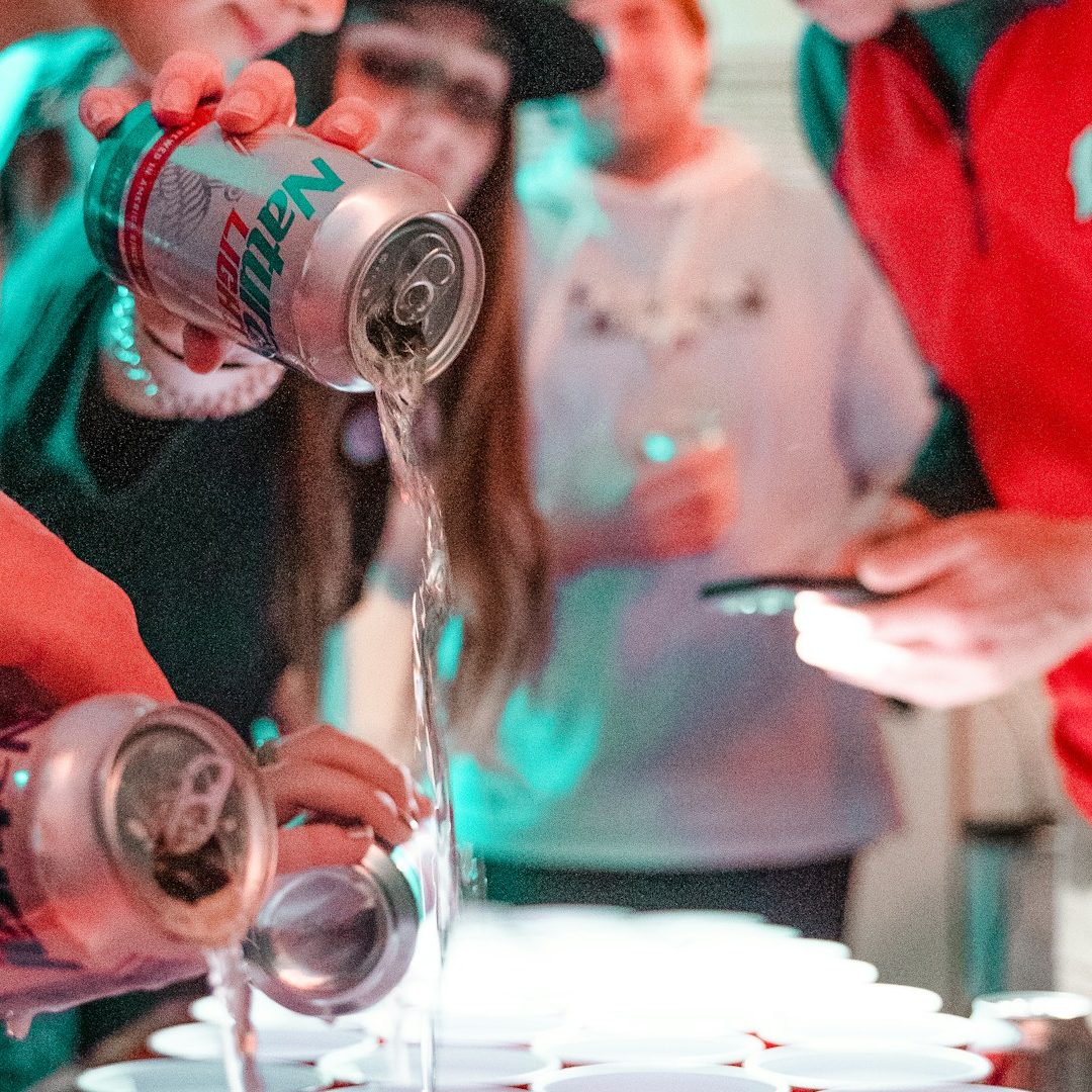 Buche jetzt deine BU-Beratung – Schnell & Kostenfrei ! Junge Menschen gießen Bier aus Dosen in Becher auf einem Tisch in feierlicher Umgebung. Berufsunfähigkeitsversicherung bei Alkohol & Drogen?