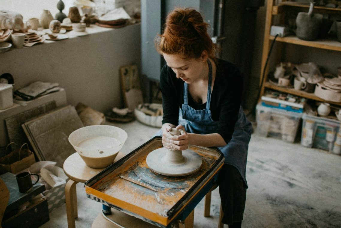 Frau formt eine Tasse auf einer Töpferscheibe in einem Atelier.