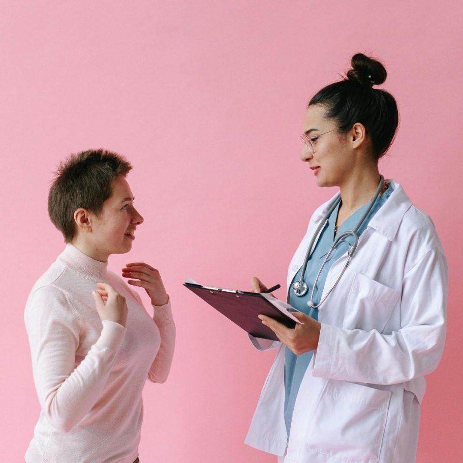 Ärztin im weißen Kittel spricht mit Patientin vor pinkem Hintergrund. BU Diagnosen & Vorerkrankung