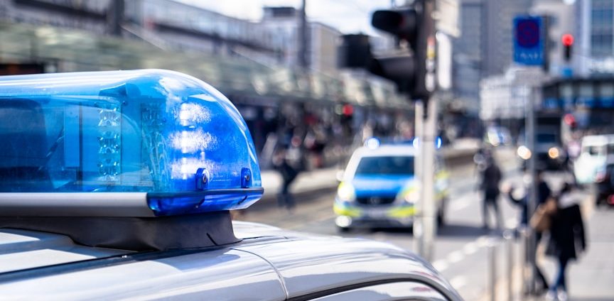 BU für Beamte Blaulicht auf einem Polizeiwagen, Menschen und Fahrzeuge im Hintergrund zur BU für Beamte