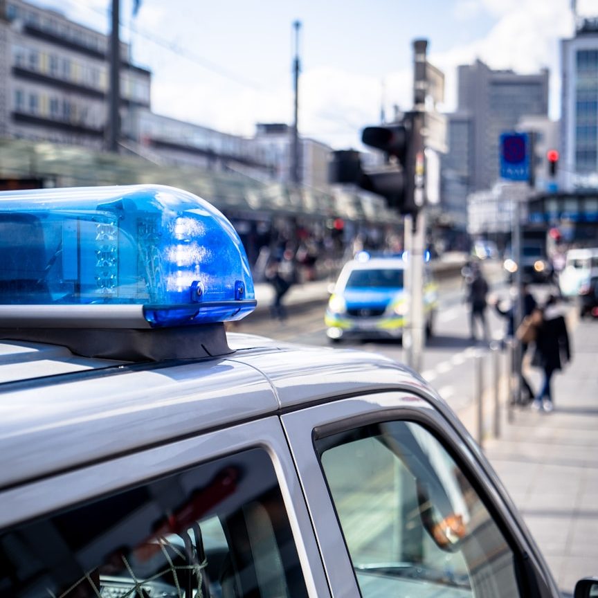 BU und Beamte Blaulicht auf einem Polizeiauto, Menschen und Fahrzeuge auf einer Stadtstraße zur Berufsunfähigkeitsversicherung