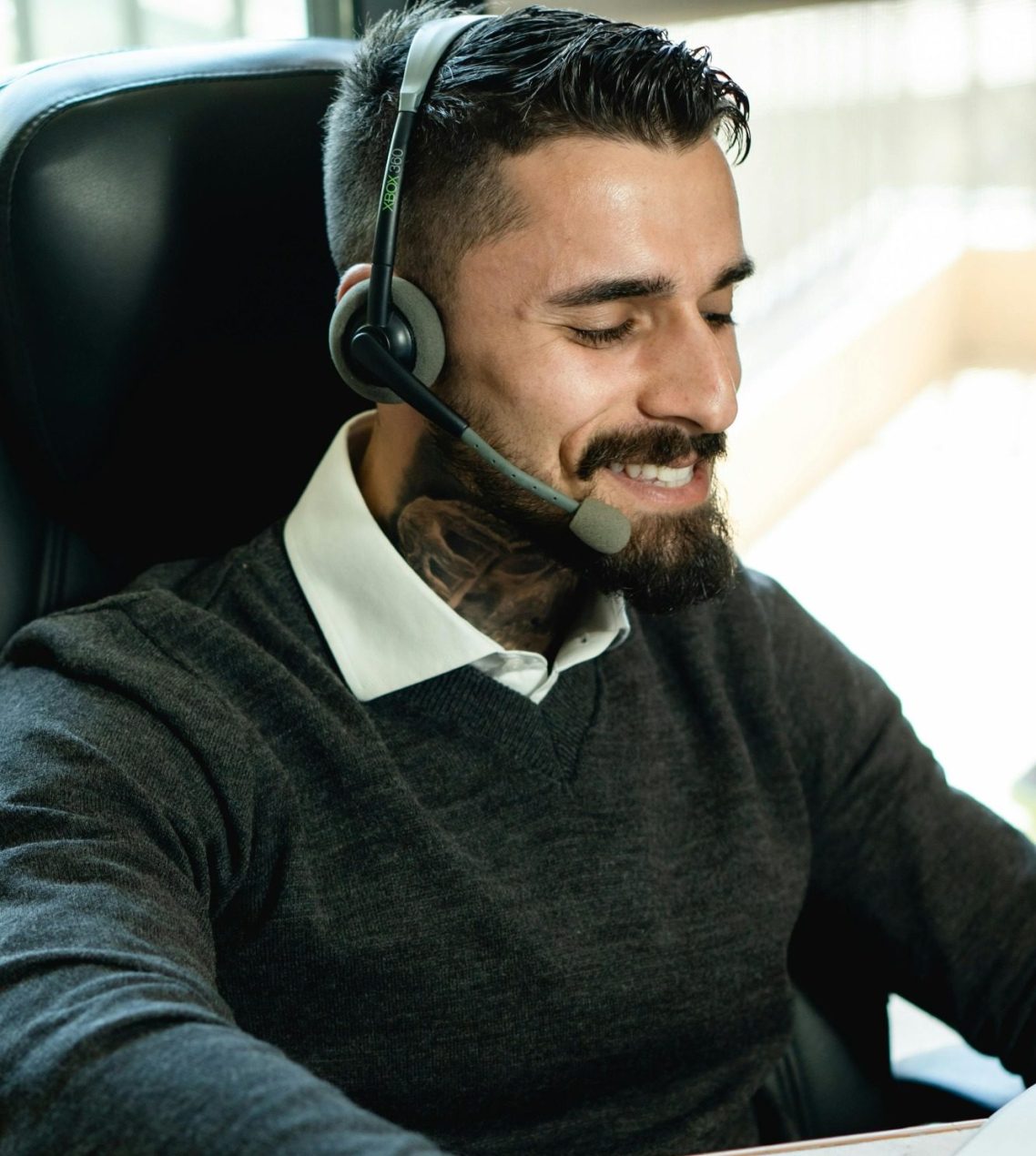Mann mit Headset am Schreibtisch, lächelt und arbeitet am Computer.