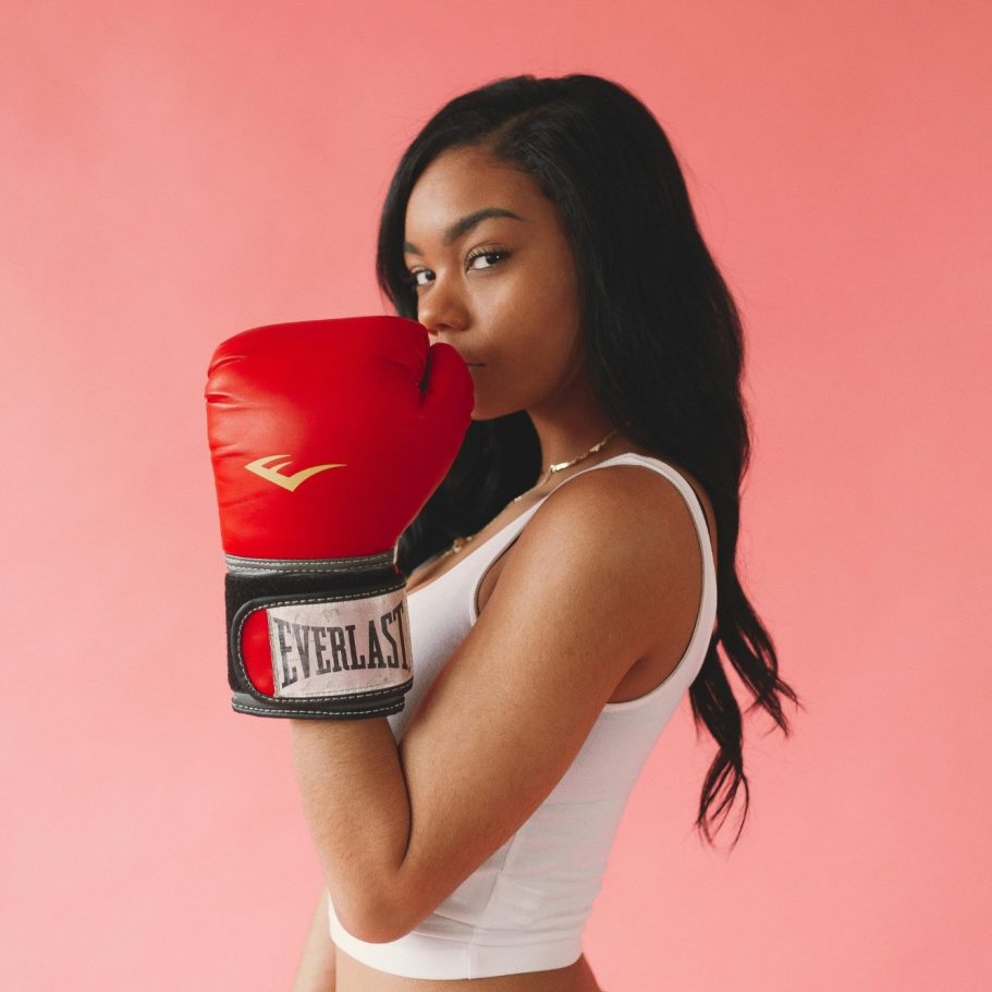 Junge Frau in Sportbekleidung trägt rote Boxhandschuhe vor pinkem Hintergrund. BU bei Hobbys, Freizeit & Risikosport