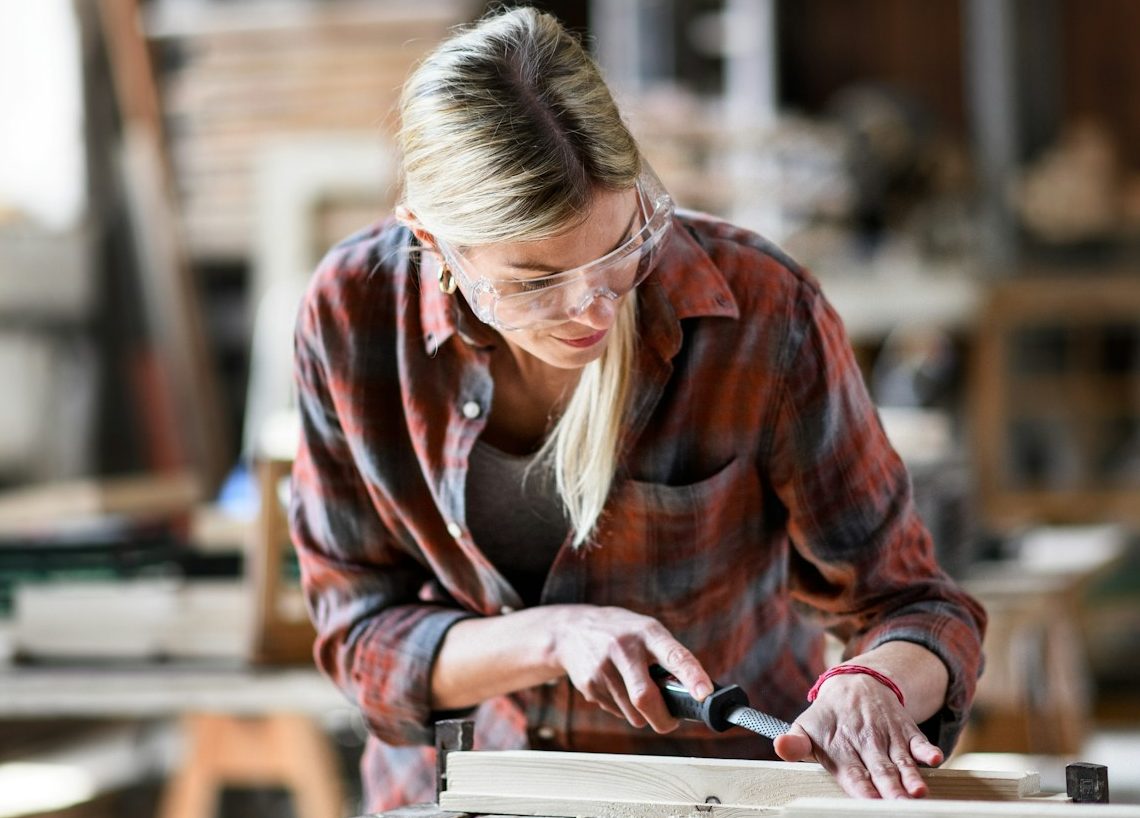 Frau mit Brille arbeitet an einem Holzprojekt in einer Schreinerei. BU für Handwerker