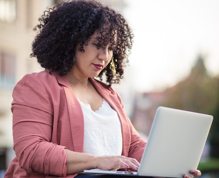 BU für Angestellte und Arbeitnehmer Frau mit lockigem Haar arbeitet am Laptop im Freien und informiert sich zur BU für Angestellte und Arbeitnehmer