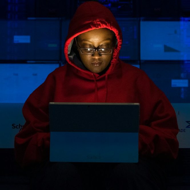 BU für IT- Berufe Person in rotem Hoodie sitzt vor einem Laptop und betrachtet den Bildschirm in dunkler Umgebung zur Berufsunfähigkeitsversicherung