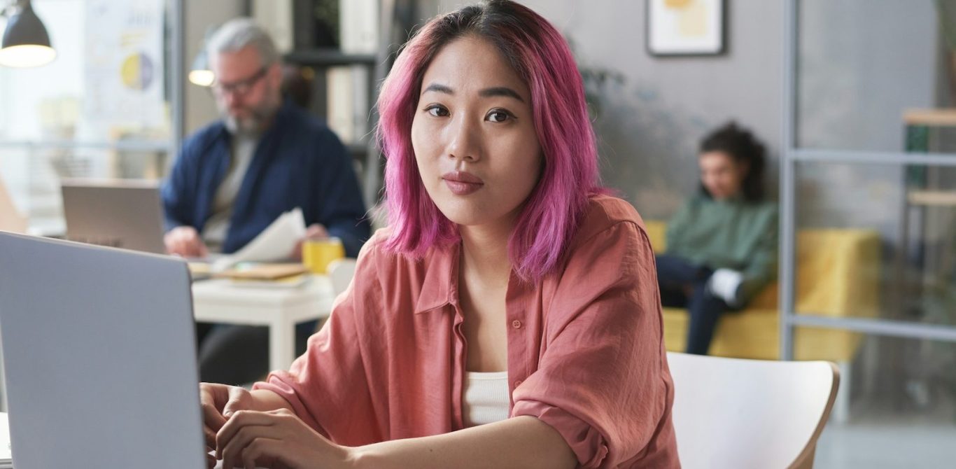 BU für Studenten Junge Frau mit pinken Haaren arbeitet am Laptop in einem modernen Café BU für Studenten