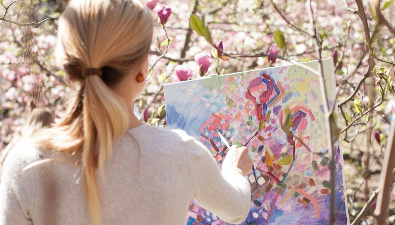 Ein Mädchen malt vor blühenden Magnolienbäumen in sanften Farben. BU für Künstler & Musiker