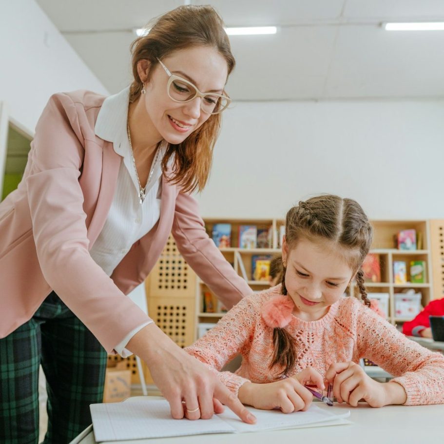 BU für Lehrer & Referendare Lehrerin hilft einem Mädchen beim Zeichnen in einem Klassenzimmer zur Berufsunfähigkeitsversicherung