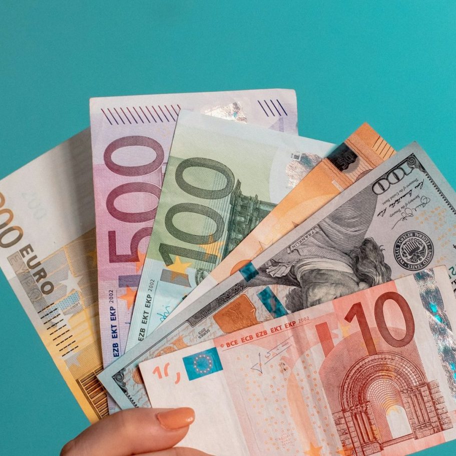Hände halten verschiedene Geldscheine, darunter Euro und US-Dollar.