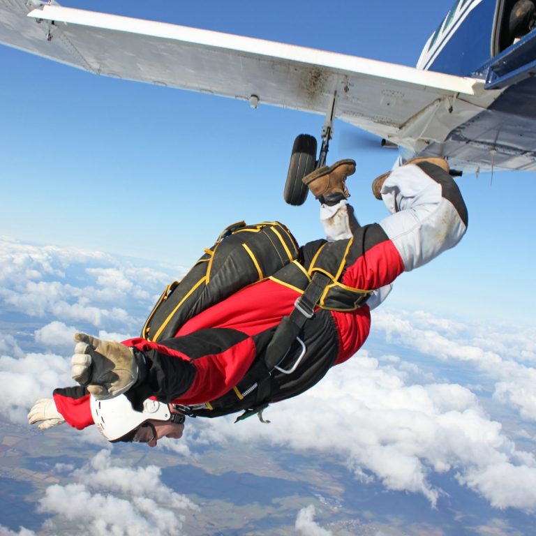 Person im Fallschirmanzug springt aus einem Flugzeug über Wolken.