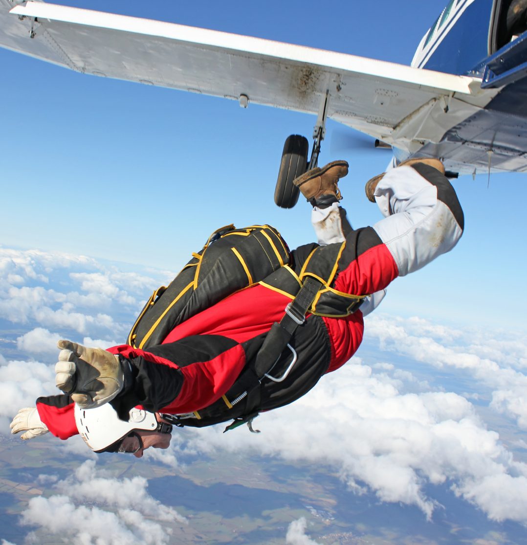 Nach Freizeitrisiken Person im Fallschirmanzug springt aus einem Flugzeug über Wolken.