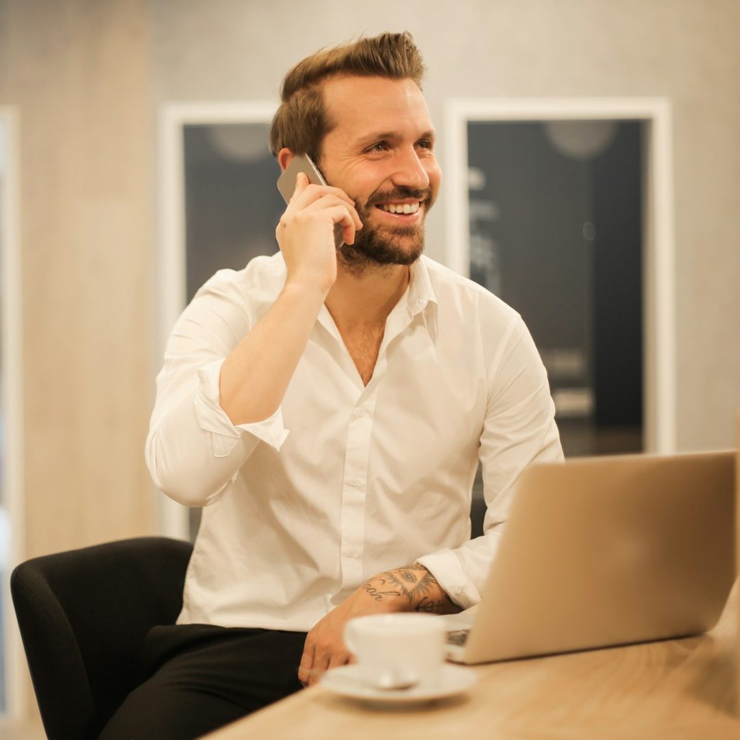 Mann in Hemd am Telefon, vor Laptop in moderner Büroumgebung.
