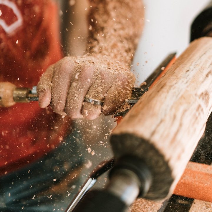 BU für Handwerker Händer bearbeiten Holz mit einem Drehwerkzeug, Späne fliegen herum zur Berufsunfähigkeitsversicherung